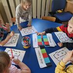 Kilkoro dzieci siedzi przy stoliku i rysują mazakami kody dla robota.