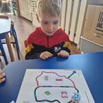 Chłopiec siedzi przy stoliku_ na którym znajduje się kartka z konturem Polski i Ozobot.