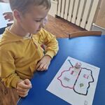 Chłopiec siedzi przy stoliku i obserwuje ozobota poruszającego się po kartce.