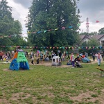 Widok placu zabaw, na nim dużo dzieci i rodziców. Ozdobiony girlandami i balonami.