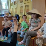 Dziewczynka w kapeluszu chińskim na głowie siedzi wśród kolegów.