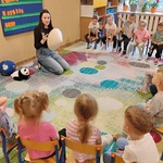 Kobieta pokazuje dzieciom siedzącym na krzesełkach chiński kapelusz.