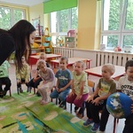 Przedszkolaki siedzą na krzesełkach i podają sobie piłkę w kształcie kuli ziemskiej.