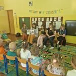 Dzieci i panie siedzą na krzesełkach_ jedna z pań trzyma otwartą książkę.