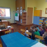 Grupa dzieci siedzi na dywanie i ogląda prezentację.