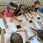 Grupa przedszkolaków próbuje pisać piórem szlaczki.