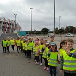 Grupa przedszkolaków stoi pod budynkiem Stadionu Miejskiego Chorten Arena.