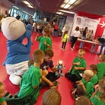 Grupka dzieci siedzi na podłodze ogląda pokaz robotów.