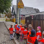 grupa dzieci w kamizelkach odblaskowych stoi wzdłuż płotu.