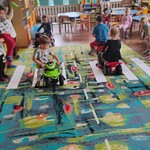 sala przedszkolna_ dzieci jeżdzą samochodami po ulicy zrobinej na dywanie.
