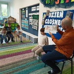 Mężczyzna siedzący z dziewczynką pokazuje dzieciom ilustracje w książce.
