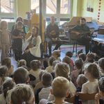 Dzieci stoją przy muzykach_ dziewczynka śpiewa do mikrofonu.