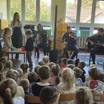 Dwoje dzieci stoi przy muzykach i trzymają miseczki.