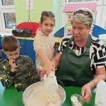 Dziewczynka z pomocą pani miksuje ciasto.