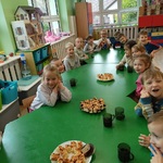 Przedszkolaki siedzą przy stolikach na których stoi upieczone ciasto.