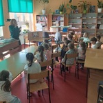 Dzieci siedzą przy stoikach, słuchają co mówi pani bibliotekarka 