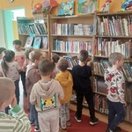 Grupa dzieci stoi między półkami w wypożyczali, ogląda księgozbiory biblioteki.