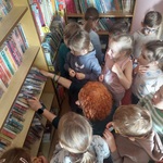 Grupa dzieci stoi między półkami w wypożyczali, ogląda księgozbiory biblioteki.