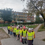 Grupa dzieci w kamizelkach odblaskowych stoi przed budynkiem szkoły