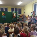 Dzieci siedzą i oglądają grę aktora i pacynkę.