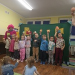 Kilkoro dzieci prezentuje swoje pacynki stojąc na środku sali.