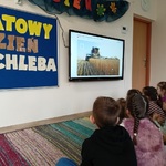 Dzieci siedzą na dywanie i oglądają film na monitorze.