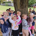Dzieci z grupy III przytulają się do drzewa, widać uśmiechnięte buzie 