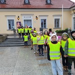 Przedszkolaki w kamizelkach odblaskowych idą parami z Ratusza.
