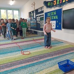 Dzieci stoją w dwóch rzędach, jedna dziewczynka trafią kasztanem do celu