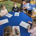 Dzieci siedzą przy stolikach i kolorują pola w kodzie binarnym.