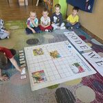 Grupa dzieci siedzi na dywanie_ a chłopiec programuje Genibota.