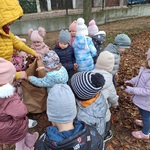 Dzieci wrzucają liście do papierowego worka trzymanego przez osobę dorosłą.