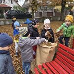 Kilkoro dzieci stoi przy papierowym worku_ trzymając w rękach liście.