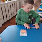 dziecko przy stoliku_ przykleja plasteline do papierowej dyni_ zwija rulon plasteliny.