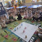 Dziewczynka układa karty do programowania robota Genibot_ grupa dzieci siedzi wokół maty.