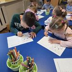 Dzieci siedzą przy stolikach i wykonują na kartkach zadania związane z robotem.