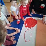 Dzieci siedzą przy stoliku w grupie_ malują farbami po brystolu_ powstaje flaga Polski