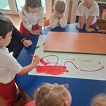 Dzieci siedzą przy stoliku w grupie_ chłopiec trzyma pędzel i maluje po białym brystolu_ powstaje flaga Polski