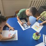 Trzech chłopców siedzi przy stoliku i rysuje pikselowe obrazki.