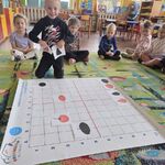 Dzieci siedzą na dywanie wokół maty_ chłopiec prezentuje pasujące do siebie obrazki.