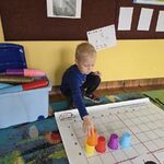 Chłopiec układa kolorowe kubeczki wg jesiennego kodu.
