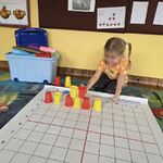 Dziewczynka układa kolorowe kubeczki wg kodu umieszczonego na tablicy.