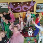 Na środku dywanu stoją roboty_ a wokół nich dzieci tańczą i machają rękami.