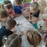 Dzieci na dywanie układają a dużych puzzli misia.