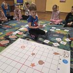Chłopiec siedzi na dywanie obok maty do kodowania i trzyma karteczki.