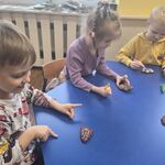 Troje dzieci siedzi przy stoliku i ozdabia pierniki.