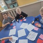 Trzech chłopców siedzi przy stoliku i patyczkiem rozsmarowują wazelinę na kartce.