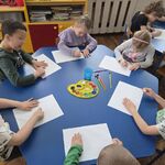 Grupa dzieci siedzi przy stoliku i rysuje świecami.