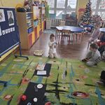 Dziewczynka siedzi przed dziećmi i pokazuje plastikowy przedmiot.
