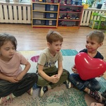 05 Chłopiec w towarzystwie kolegów siedzi na dywanie trzynając balon.jpg